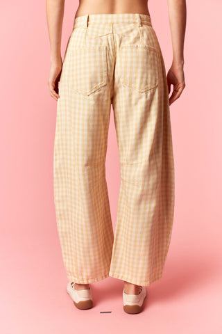 A person shown from the back wearing wide-leg cropped pants with a small gingham check pattern in pale yellow and white, paired with white shoes, against a solid pink studio background.
