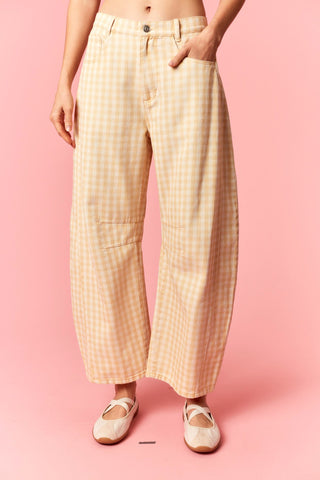 A person wearing high-waisted, wide-leg cropped pants in a pale yellow and white gingham check pattern, paired with beige ballet flats, set against a solid pink studio background.