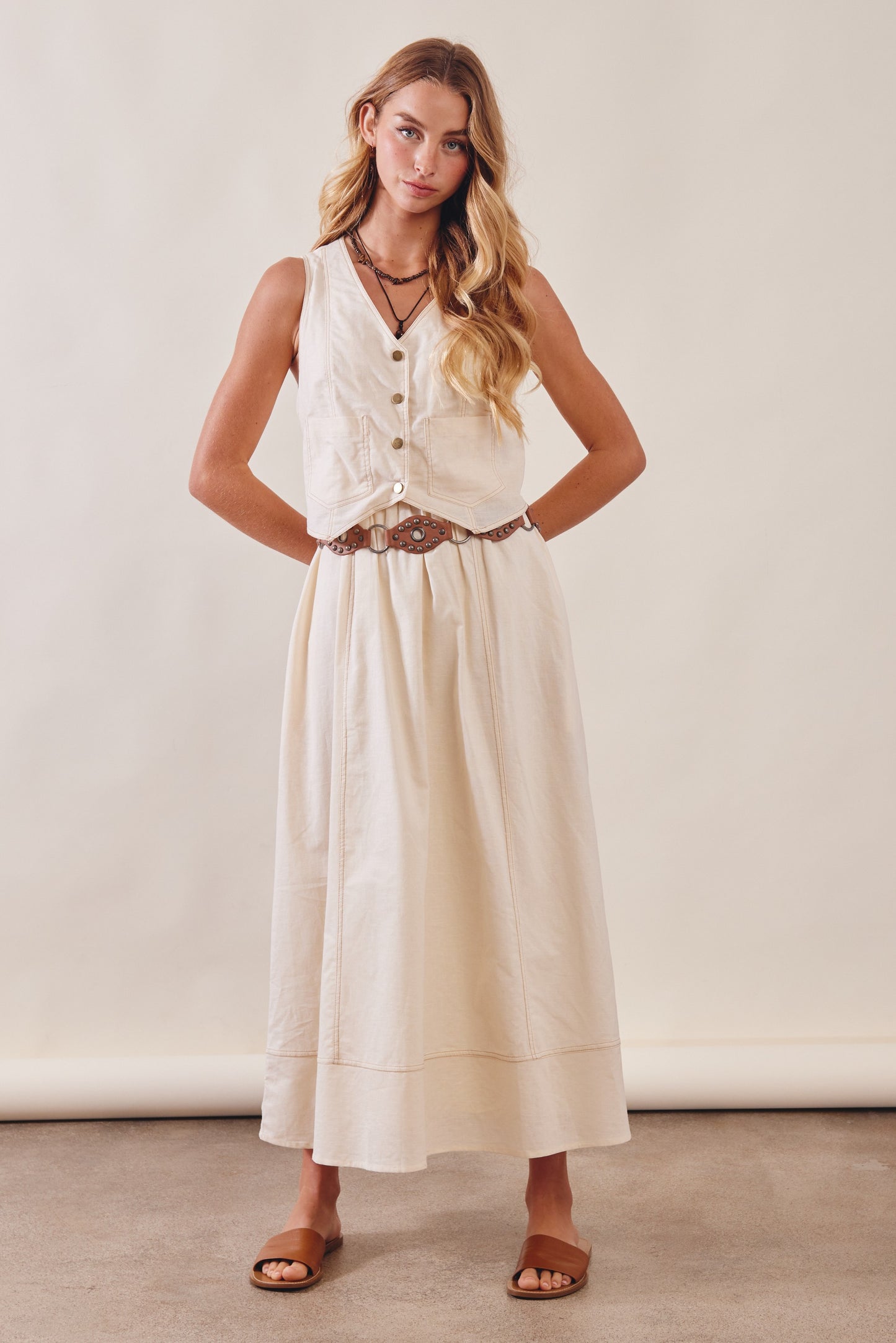 Woman wearing a white sleeveless dress with buttons on a plain background