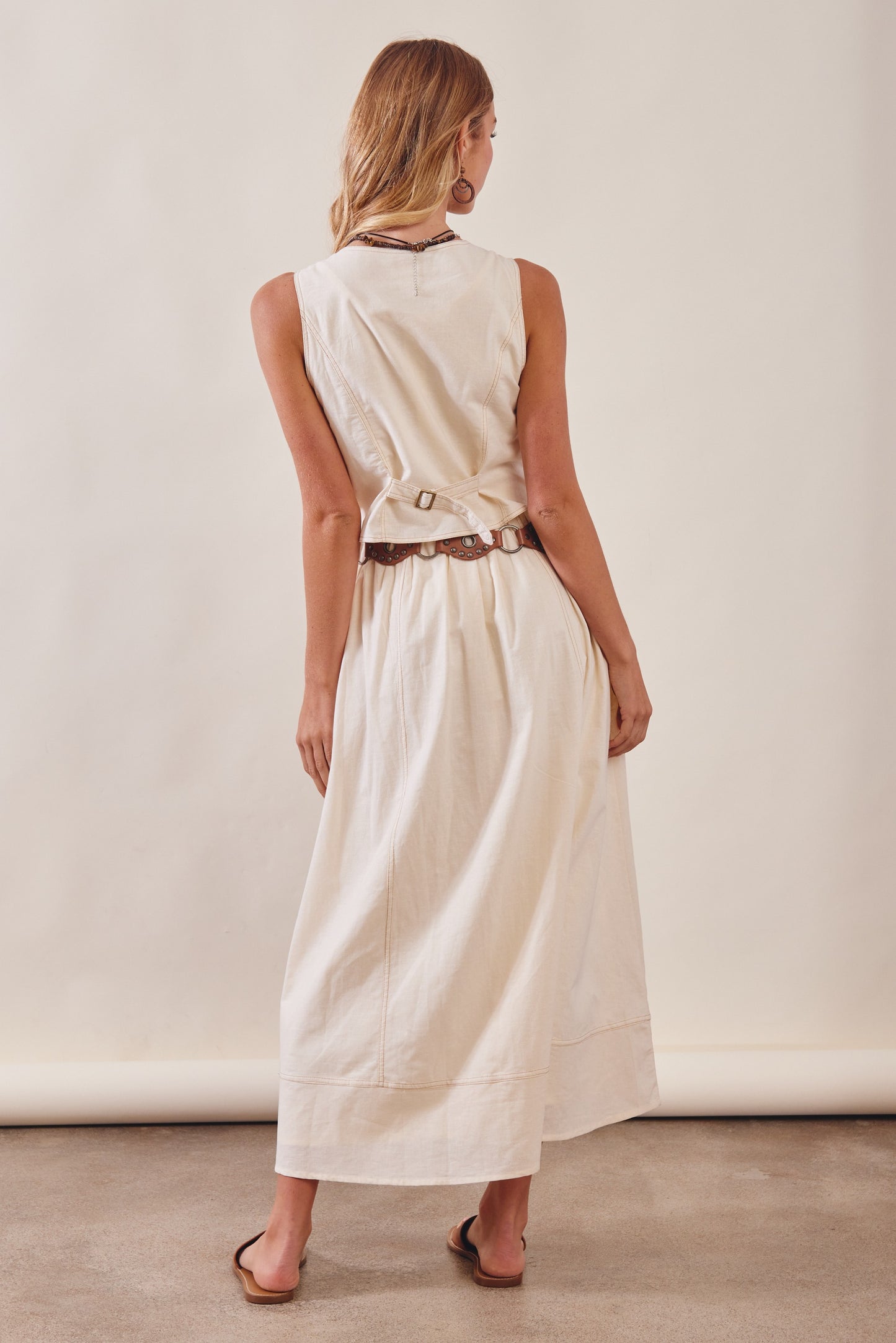 Woman wearing a beige sleeveless dress with a belt against a plain background