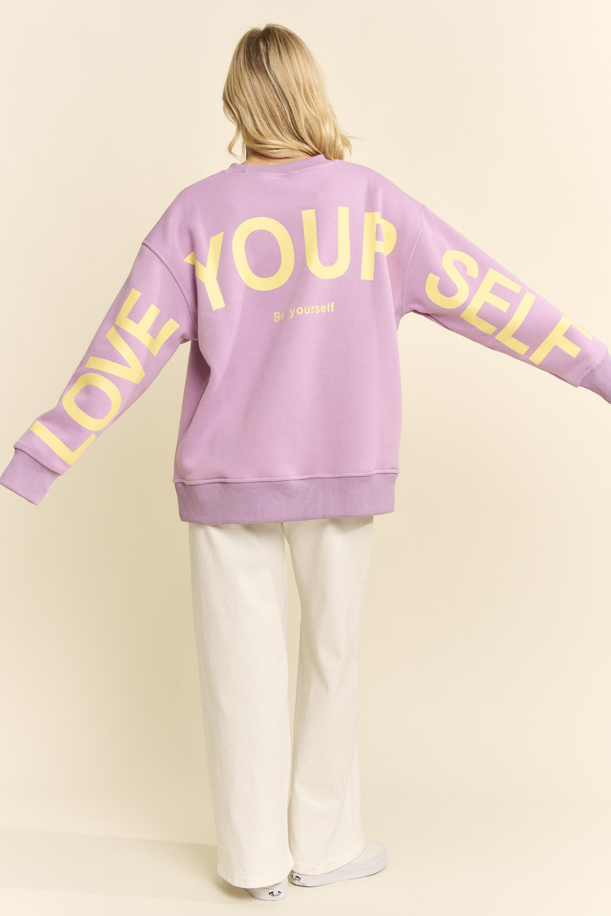 Person wearing a purple sweatshirt with 'Love Your Self' text on a plain background