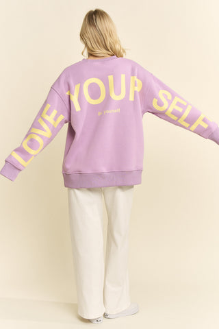 Person wearing a purple sweatshirt with 'Love Your Self' text on a plain background