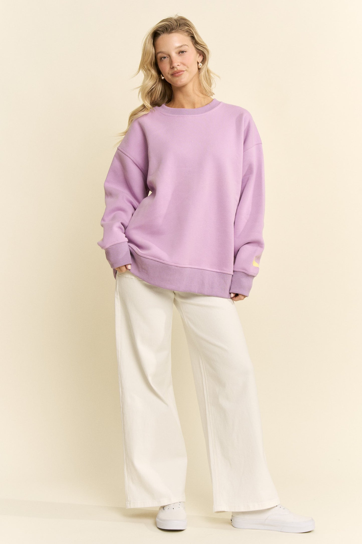 Woman wearing a purple sweater and white pants against a beige background