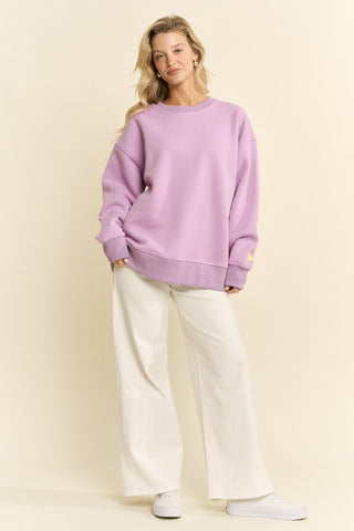 Woman wearing a purple sweater and white pants against a beige background