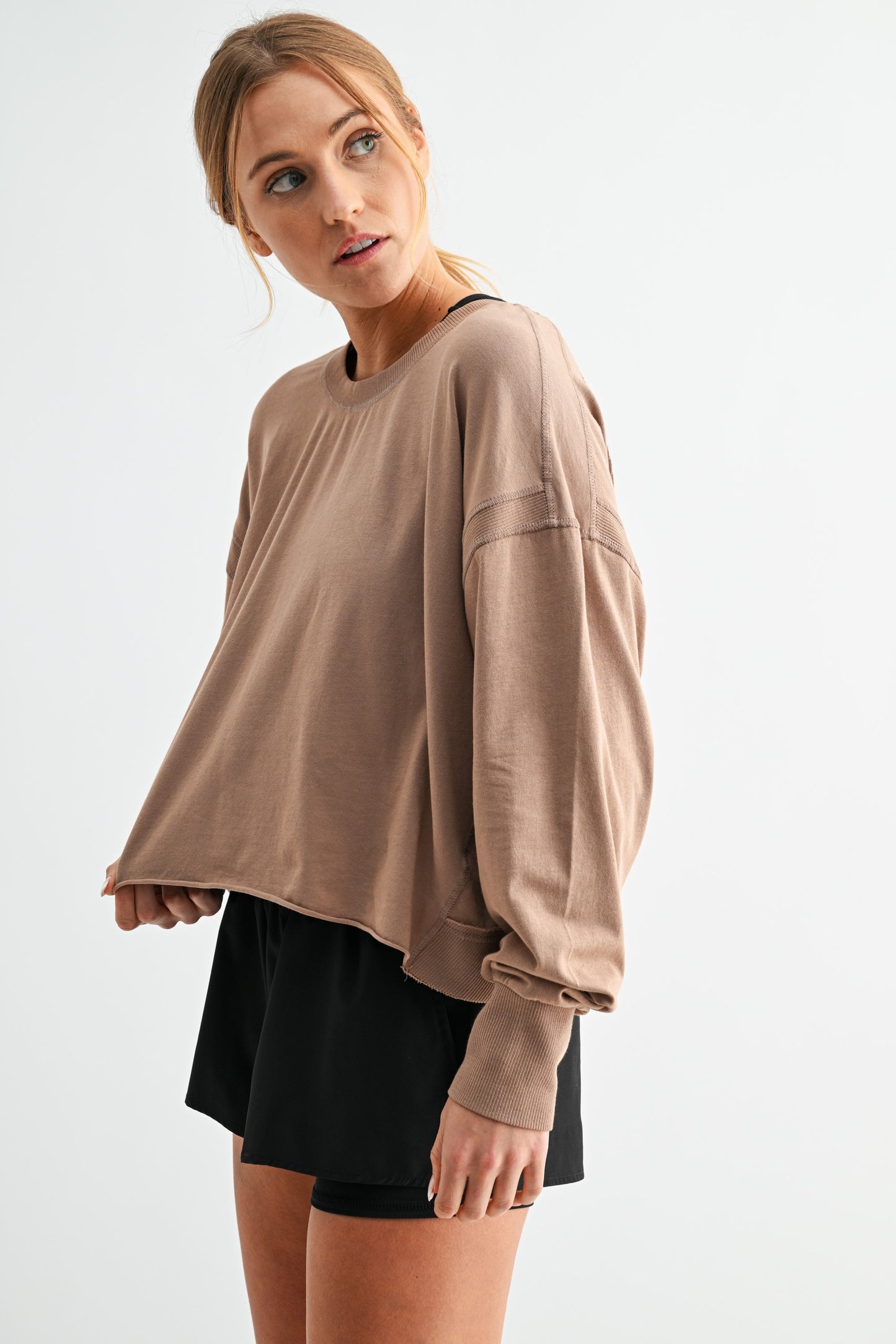 Woman wearing a beige oversized sweatshirt and black shorts on a white background