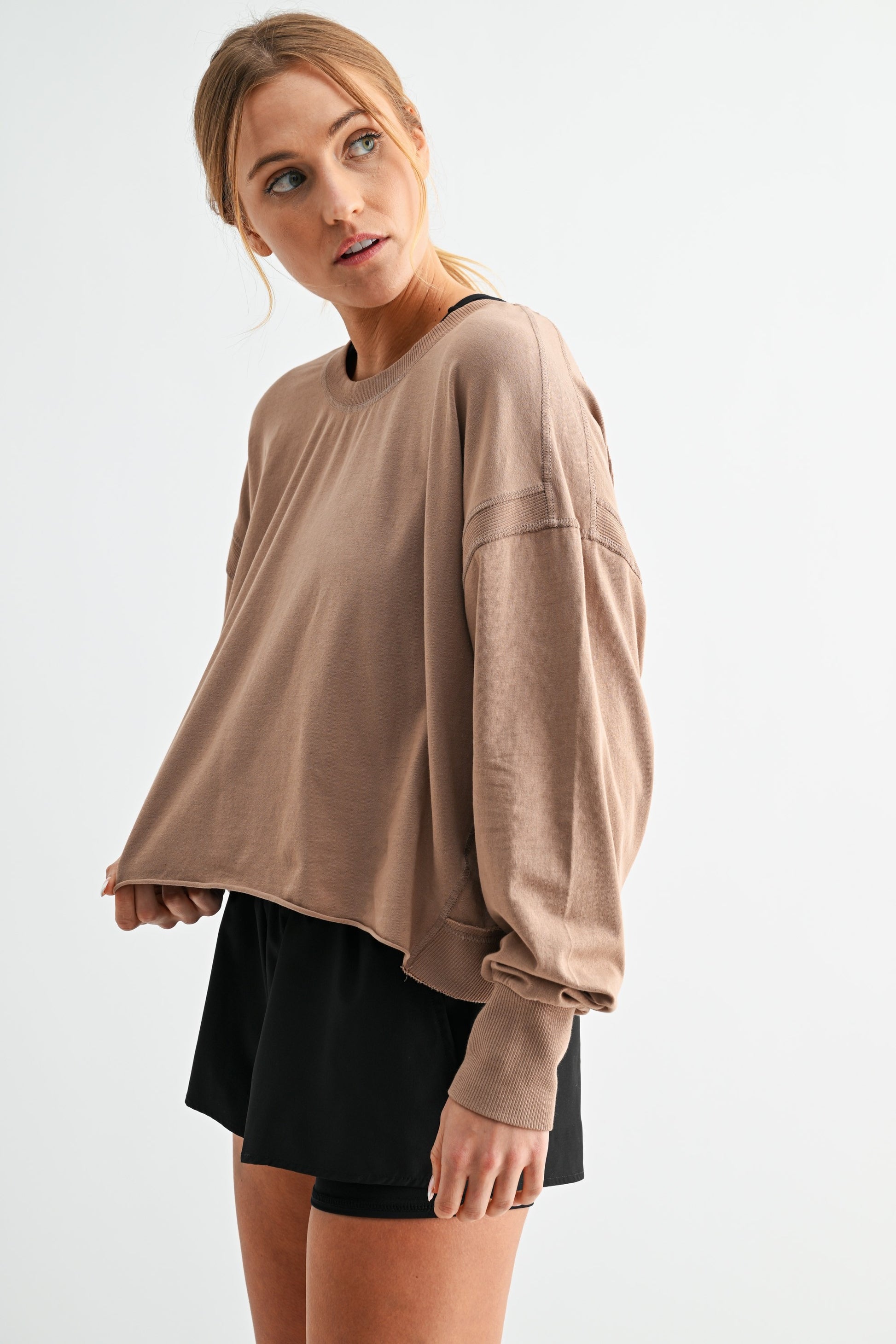 Woman wearing a beige oversized sweatshirt and black shorts on a white background