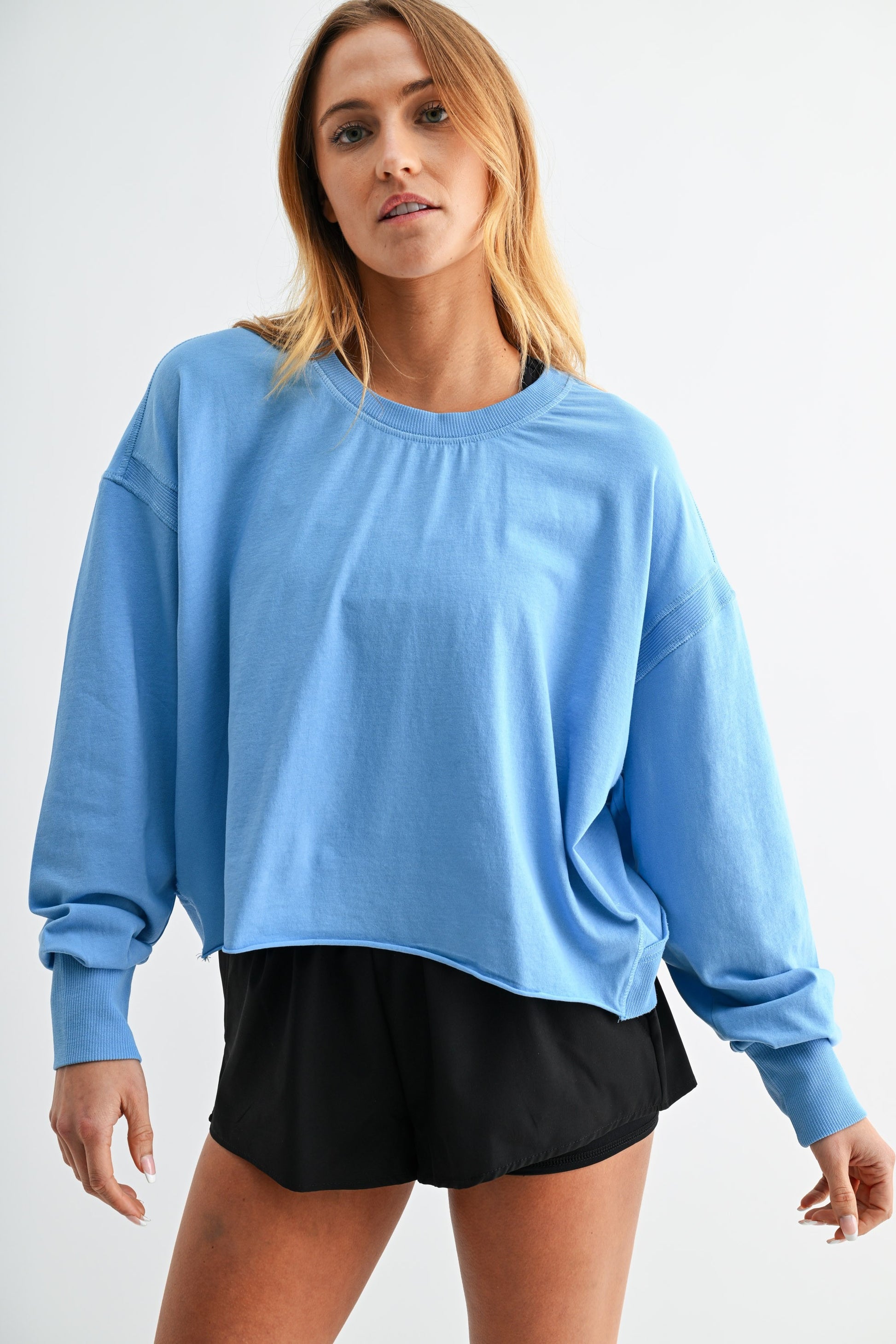 Woman wearing a blue oversized sweatshirt and black shorts on a white background