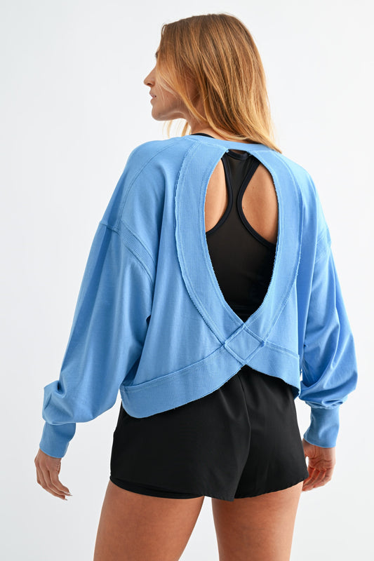 Woman wearing a light blue sweatshirt with an open back and black shorts on a white background