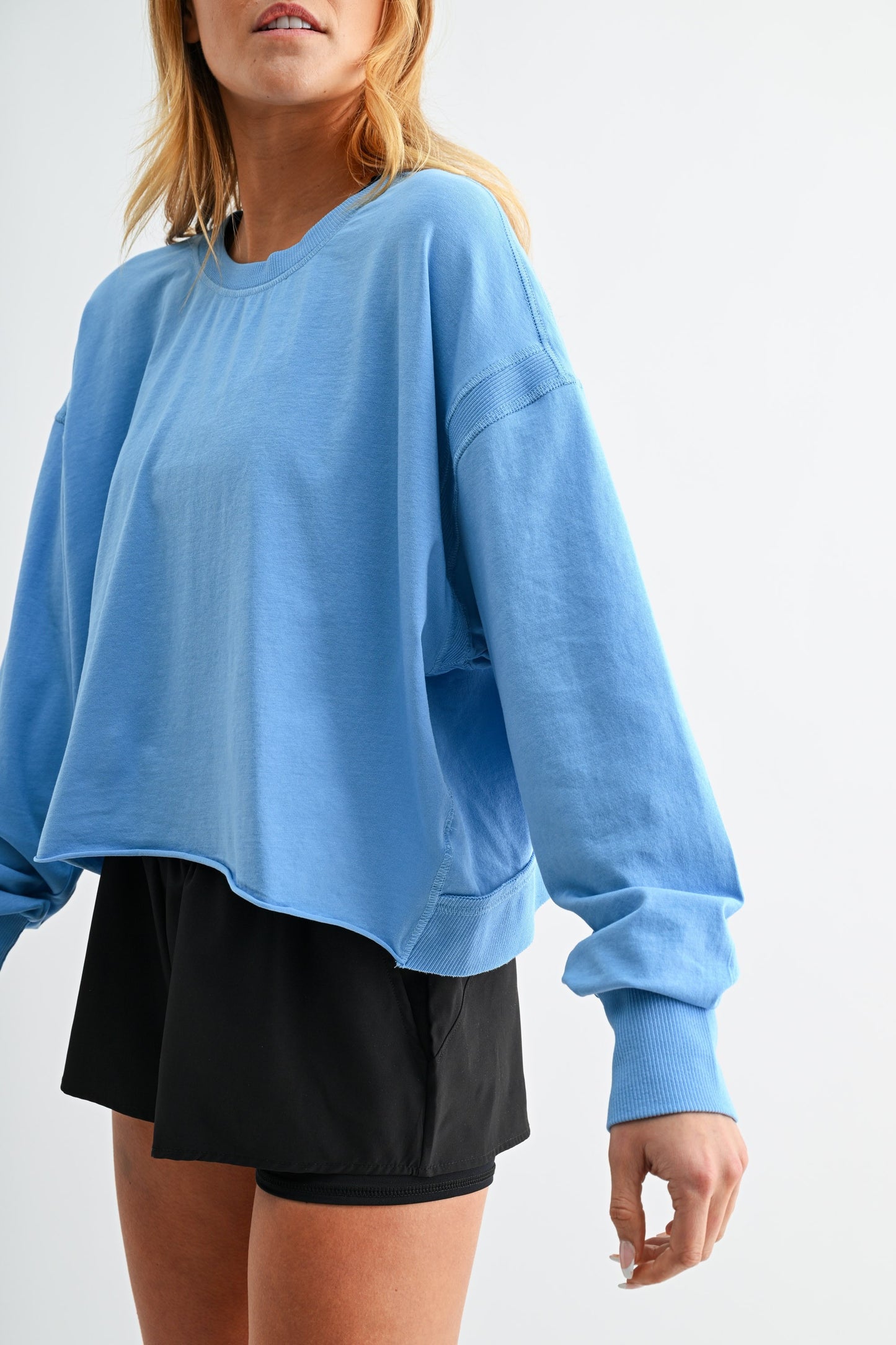 Person wearing a blue oversized sweatshirt and black shorts on a white background