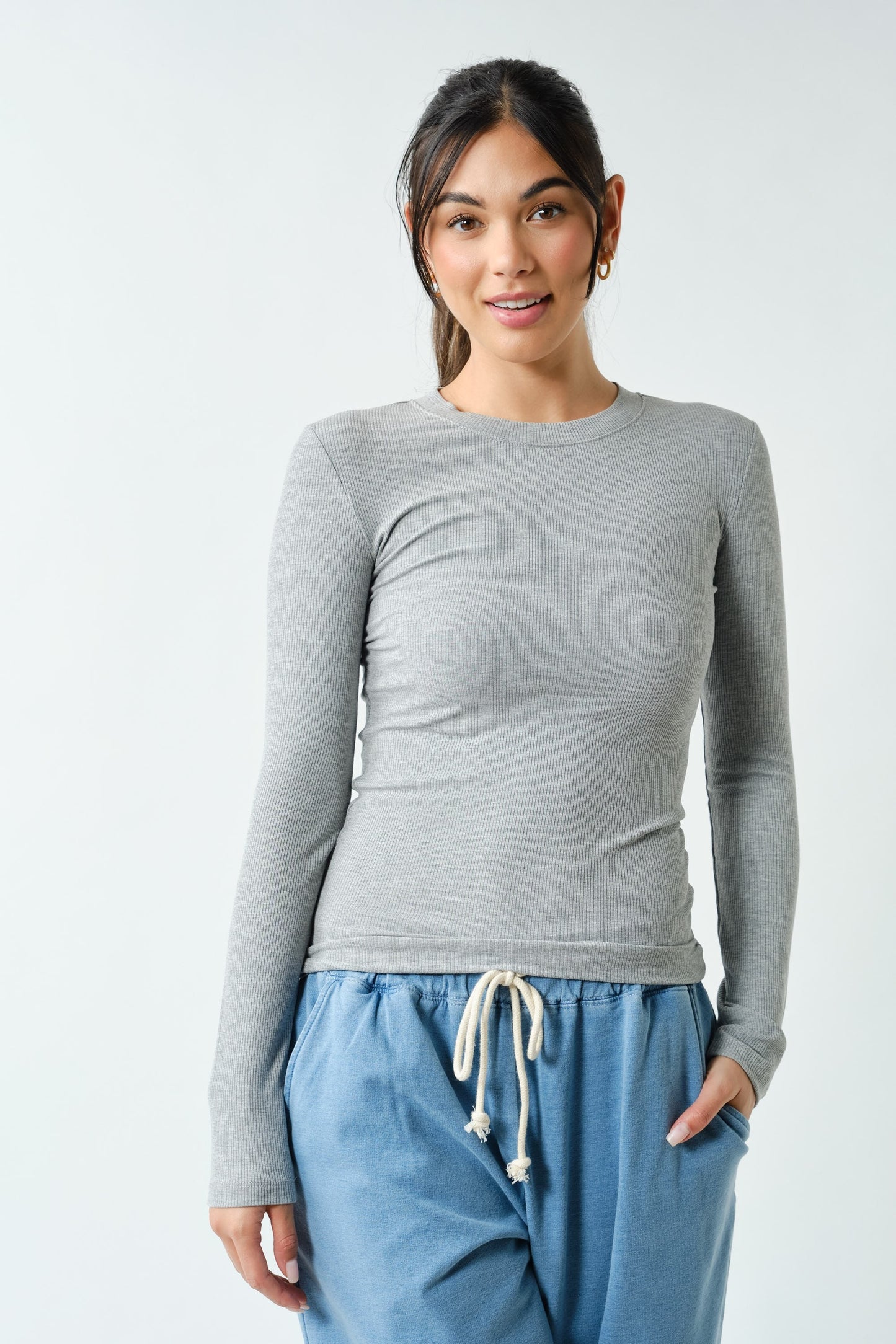 Woman wearing a gray long-sleeve top and blue pants on a white background
