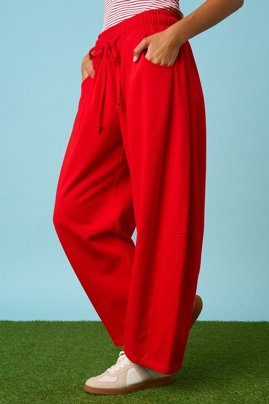 Person wearing red wide-leg pants on a grassy surface with a blue background