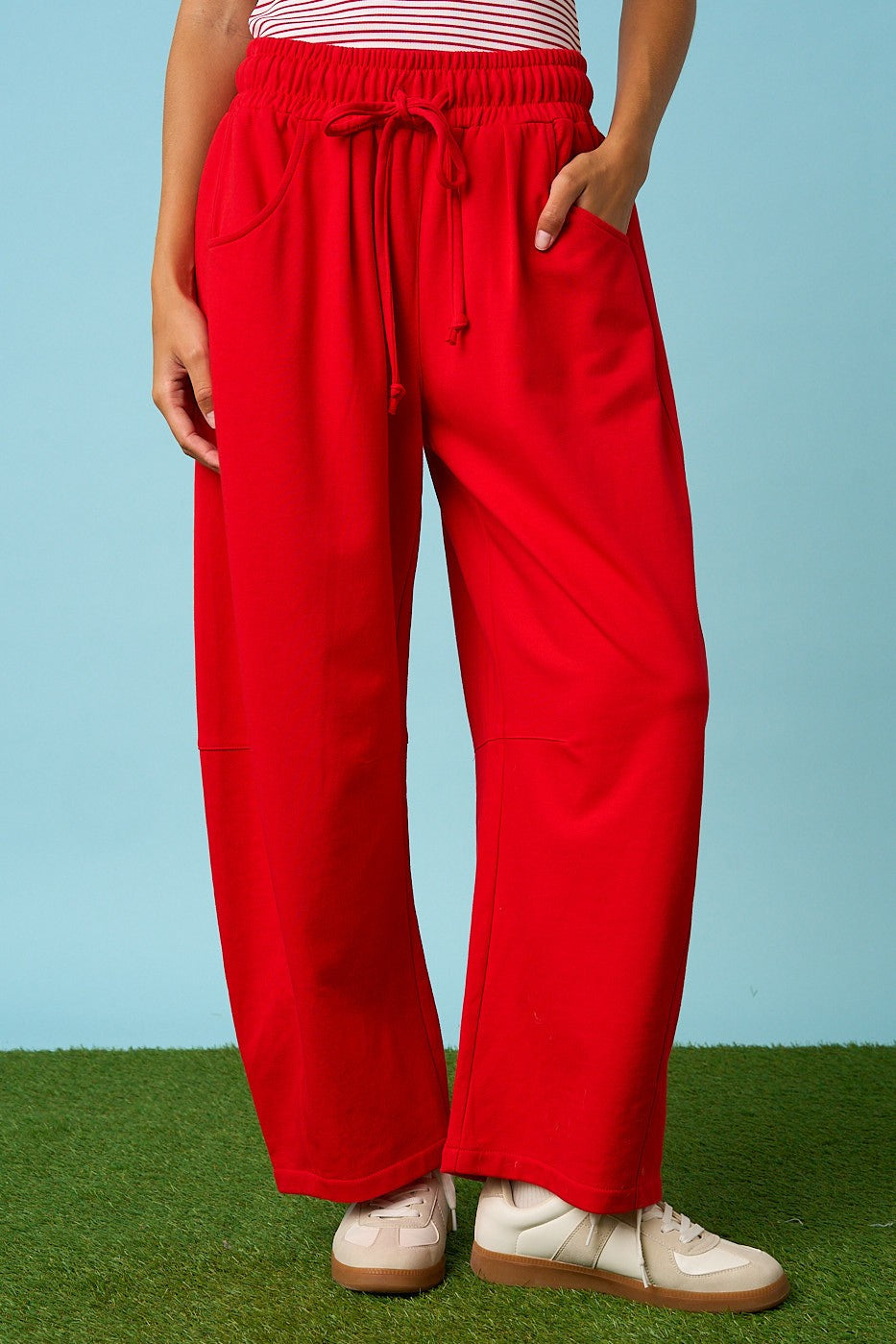 Person wearing red pants and white shoes on a grassy surface with a blue background