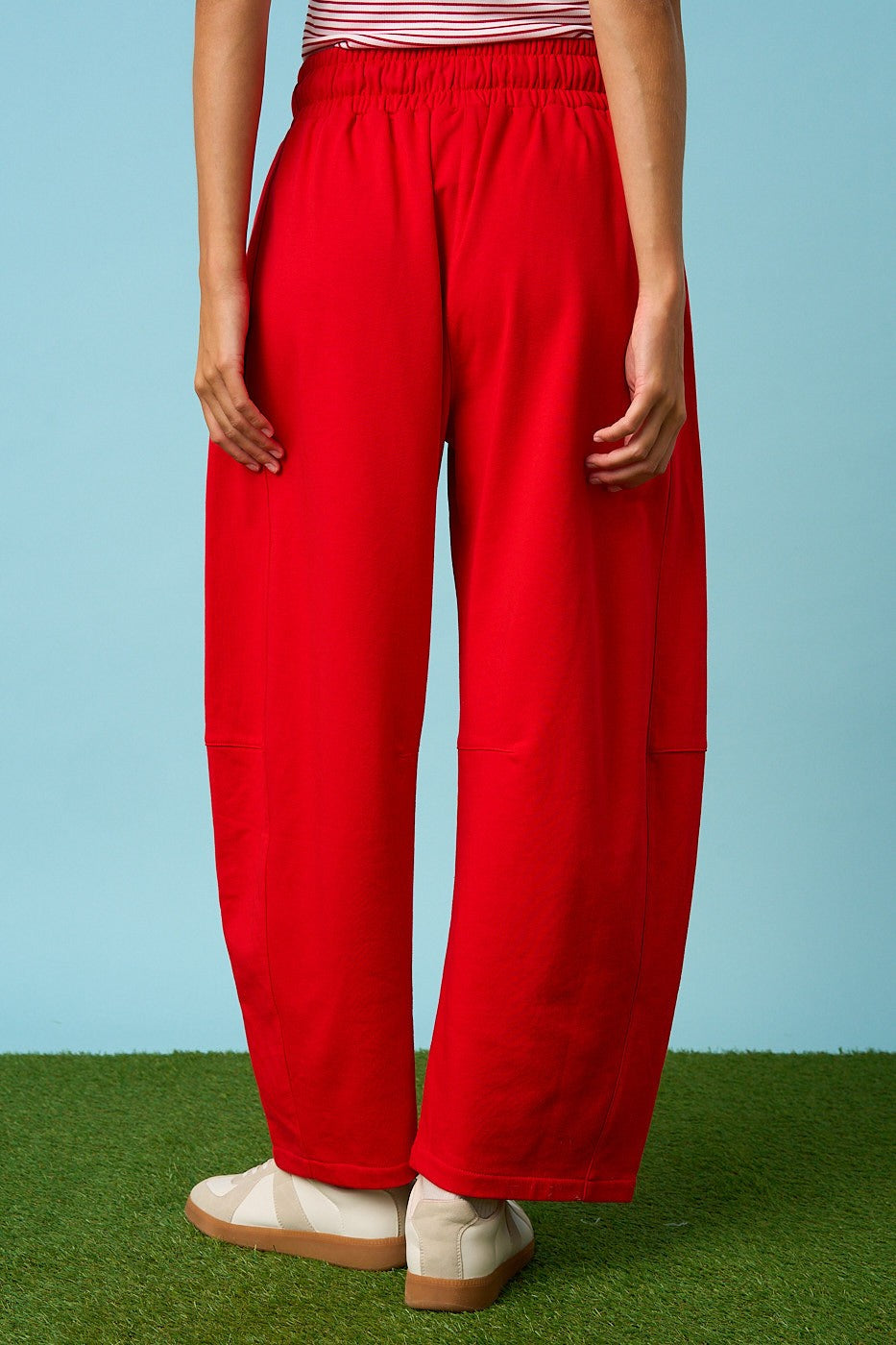 Person wearing red pants and a striped shirt on a grassy surface with a blue background