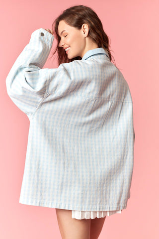 Woman wearing a light blue checkered shirt over a white dress on a pink background