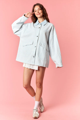 Woman wearing a light blue checkered shirt and shorts on a pink background