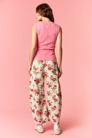 Woman wearing a pink sleeveless top and floral pants against a pink background