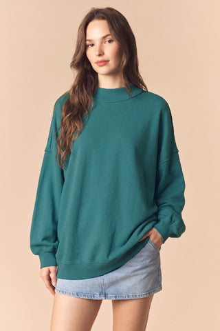 Woman wearing a teal sweater and denim skirt on a beige background