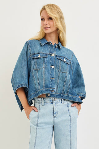 Woman wearing a blue denim jacket and jeans on a plain background