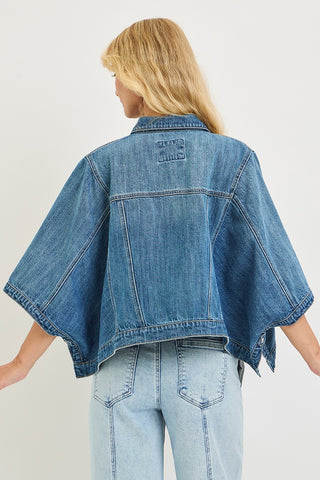Person wearing a blue denim jacket and jeans on a plain background