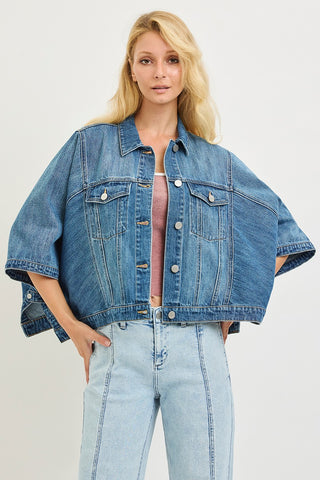 Woman wearing a blue denim jacket and jeans on a light gray background