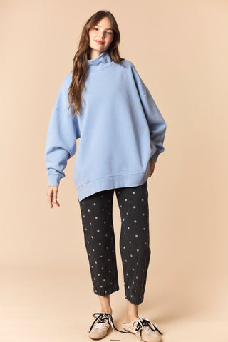 Woman wearing a light blue oversized hoodie and black pants with white patterns on a beige background