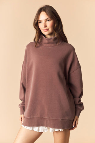 Woman wearing a brown sweatshirt over a white top on a beige background