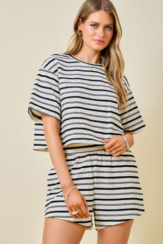 A woman modeling a matching two-piece set with a black and off-white horizontal stripe pattern, featuring a short-sleeve cropped top and matching shorts, against a solid beige background.