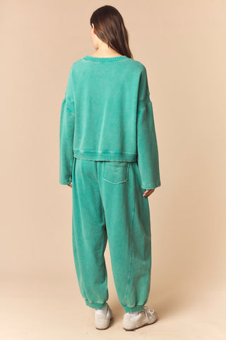 A woman viewed from behind wearing a matching mint green lounge set consisting of a cropped knit sweater and wide-leg sweatpants, paired with white sneakers, against a solid beige studio background.
