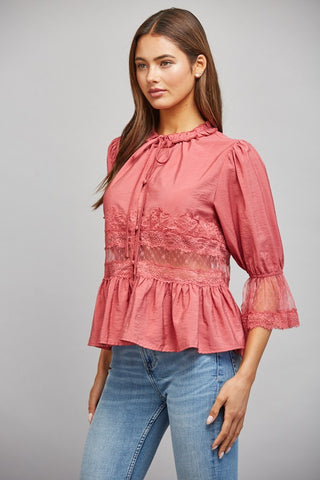 Women wearing a pink lace blouse against a neutral background.