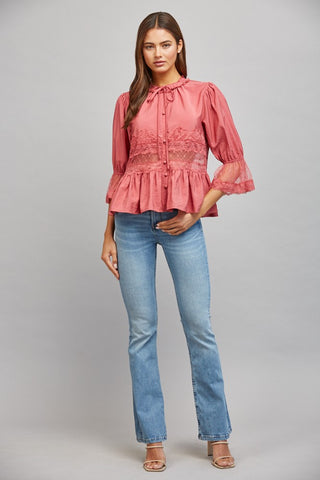 Women wearing a pink lace blouse against a neutral background.