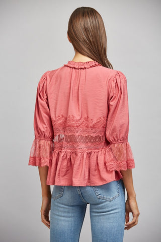 Women wearing a pink lace blouse against a neutral background.