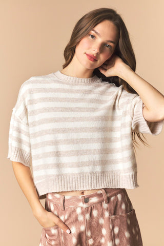 A women wearing a striped cropped sweater against a neutral background. 