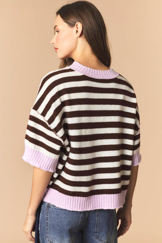 A women wearing a striped cropped sweater against a neutral background. 