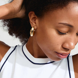 Close-up of a woman wearing gold hoop earrings with a white top.