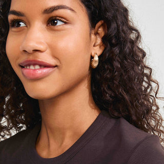 Close-up of a woman wearing gold hoop earrings with a neutral background