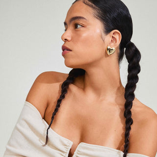 Woman with braided hair wearing a heart-shaped earring against a neutral background