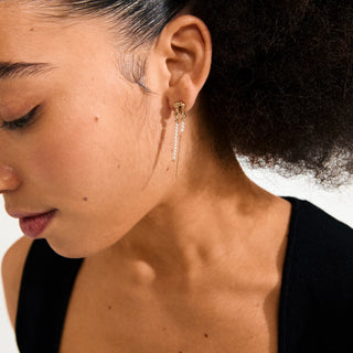 Close-up of a woman wearing a gold earring with dangling beads.