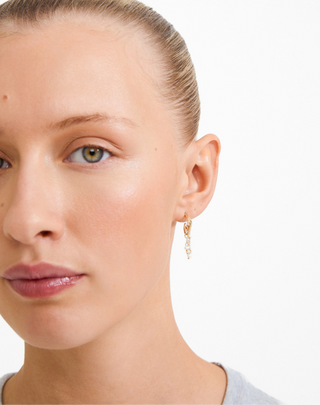 Close-up of a woman wearing gold earrings with a plain background