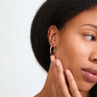 women wearing a gold hoop earring against a neutral earring. 
