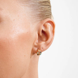 A close-up of a model's ear wearing a small gold stud earring adorned with multiple colorful round gemstones, set against a plain white background.