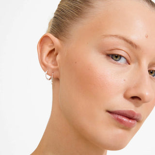 A close-up of a woman's ear wearing a delicate silver crescent hoop earring against a clean white background.