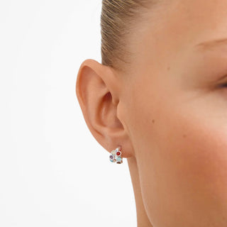 A close-up of a person's ear wearing a small silver stud earring with colorful gemstone accents, set against a plain white background.