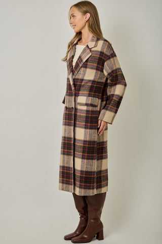Women modelling a long plaid coat against a neutral photo back drop. 