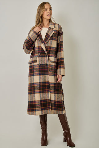 Women modelling a long plaid coat against a neutral photo back drop. 