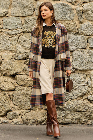 Women modelling a long plaid coat outside in front of a rock wall. 