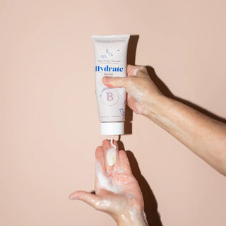 Hand holding a tube of 'Hydrate' cream against a beige background