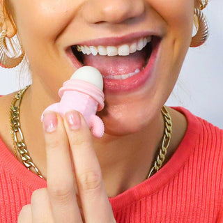 Person applying a pink lip balm to their lips with a white background