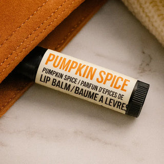 A tube of Pumpkin Spice lip balm resting on a light marble surface next to a brown suede pouch.