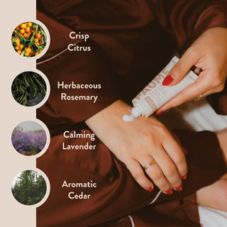 Person applying cream to wrist with scents of crisp citrus, herbaceous rosemary, calming lavender, and aromatic cedar displayed.