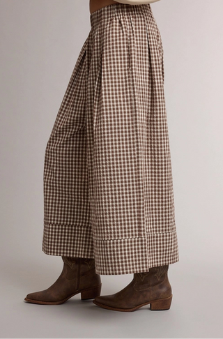 Brown and beige gingham wide-leg cropped pants with rolled cuffs, shown on a model wearing brown leather cowboy boots against a neutral studio background.